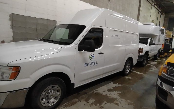 A SKATEL-liveried high-roof cargo van in the Acheson shop, the rest of the telecom fleet parked behind it.